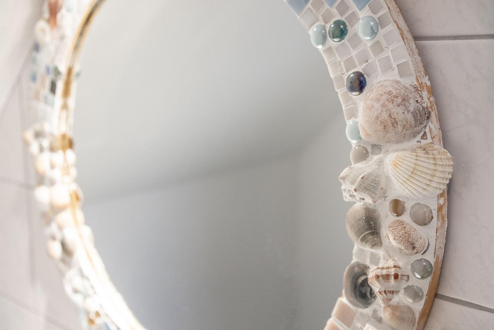 Spiegel mit Mosaikrahmen aus Muscheln und Steinen an Wand
