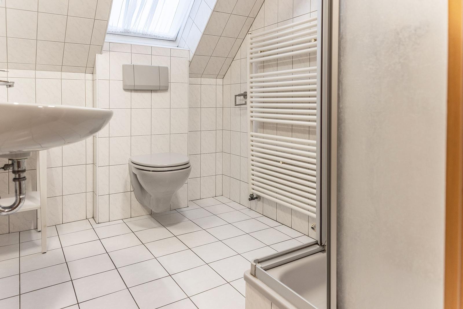 Badezimmer mit Toilette, Waschbecken und Dusche unter Dachschrägen.