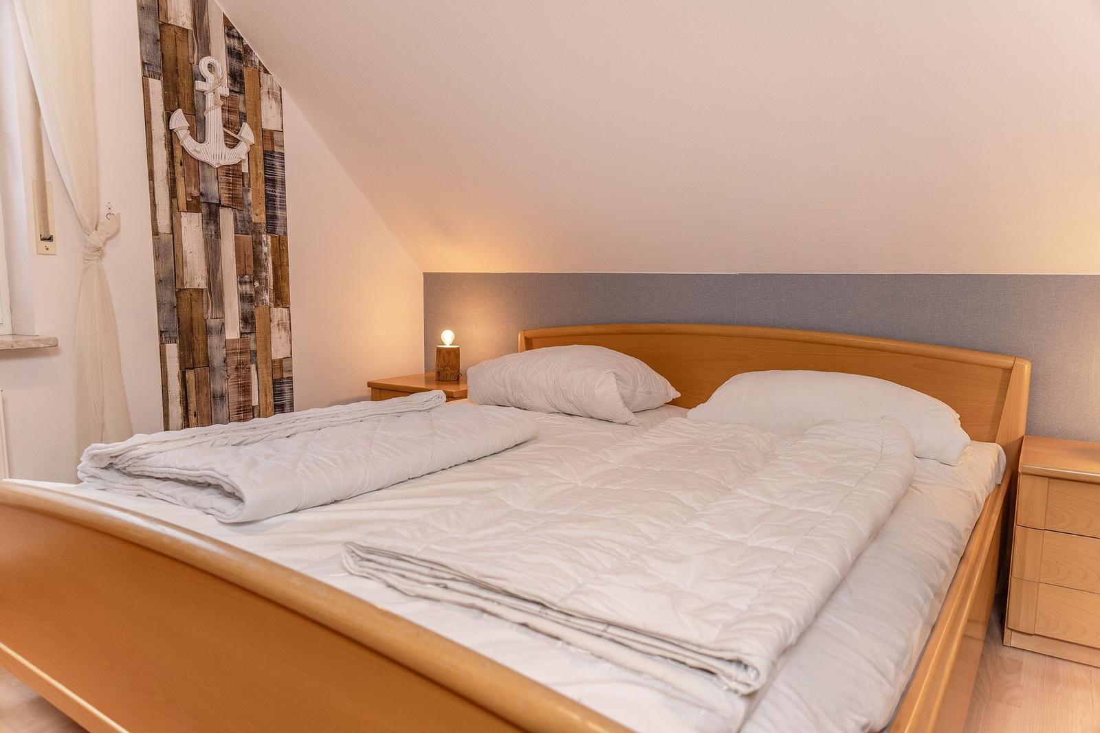 Schlafzimmer mit Doppelbett, Holzkommode und Wand mit Ankermotiv.