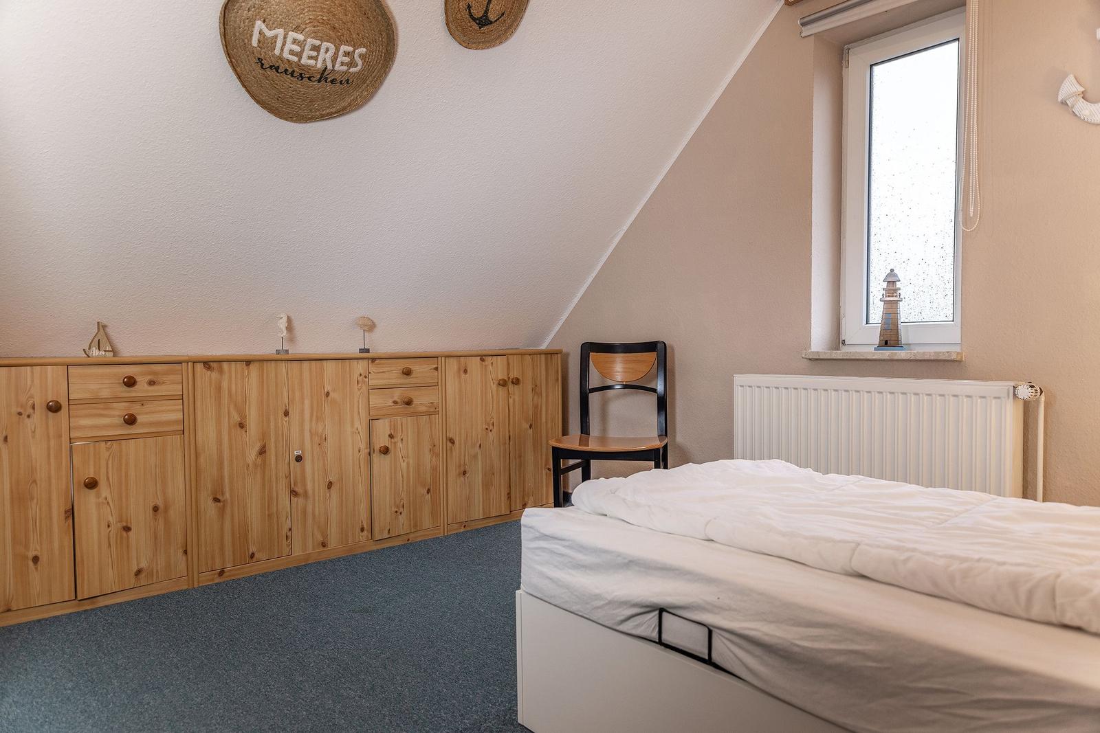 Schlafzimmer mit Bett, Holzschrank und Stuhl unter schrägem Dach