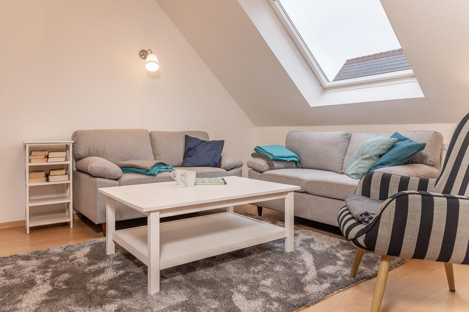 Wohnzimmer mit zwei Sofas, Couchtisch und Dachfenster. Bücherregal und Sessel sind vorhanden.