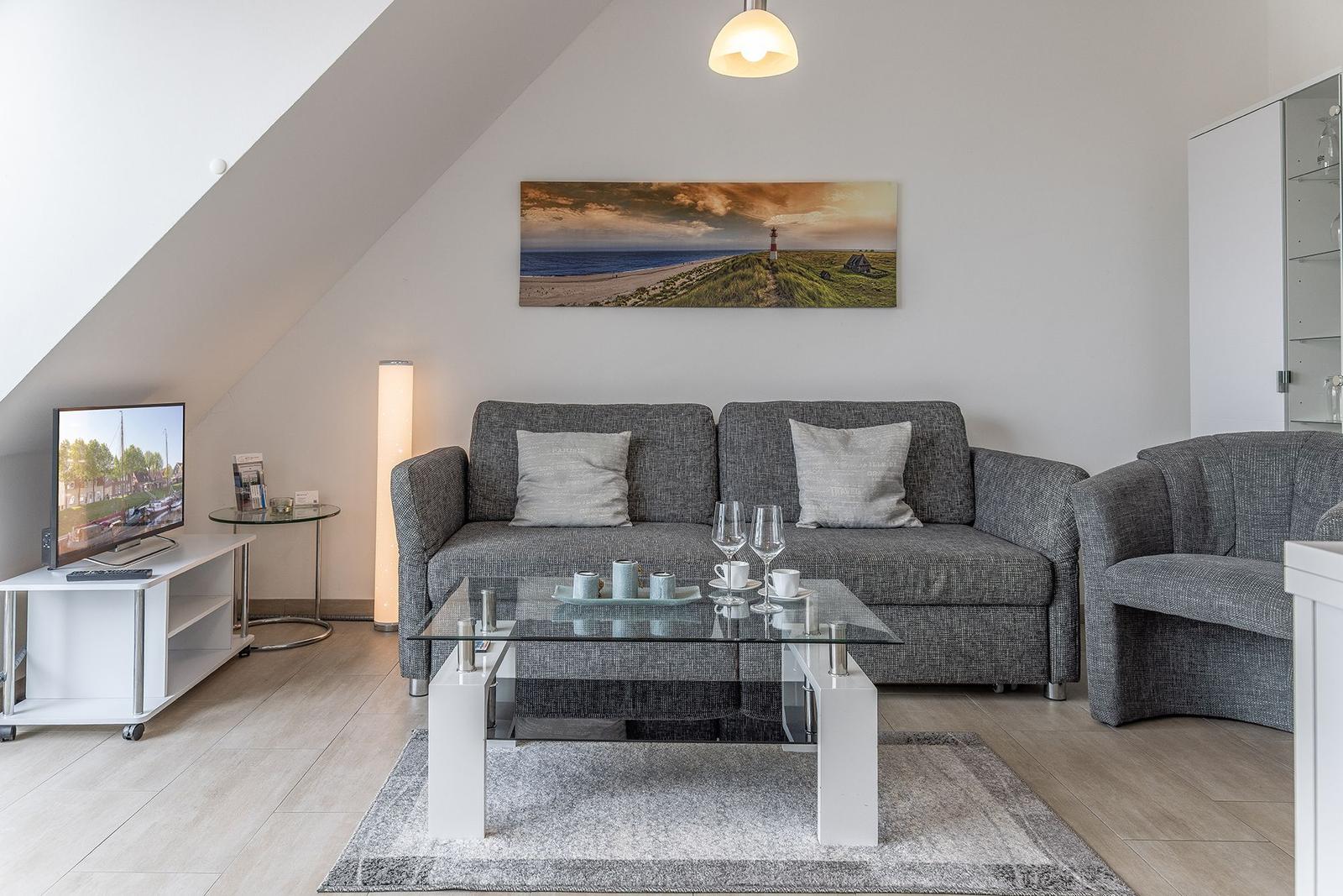 Wohnzimmer mit Sofa, Couchtisch und Fernseher unter schräger Decke.