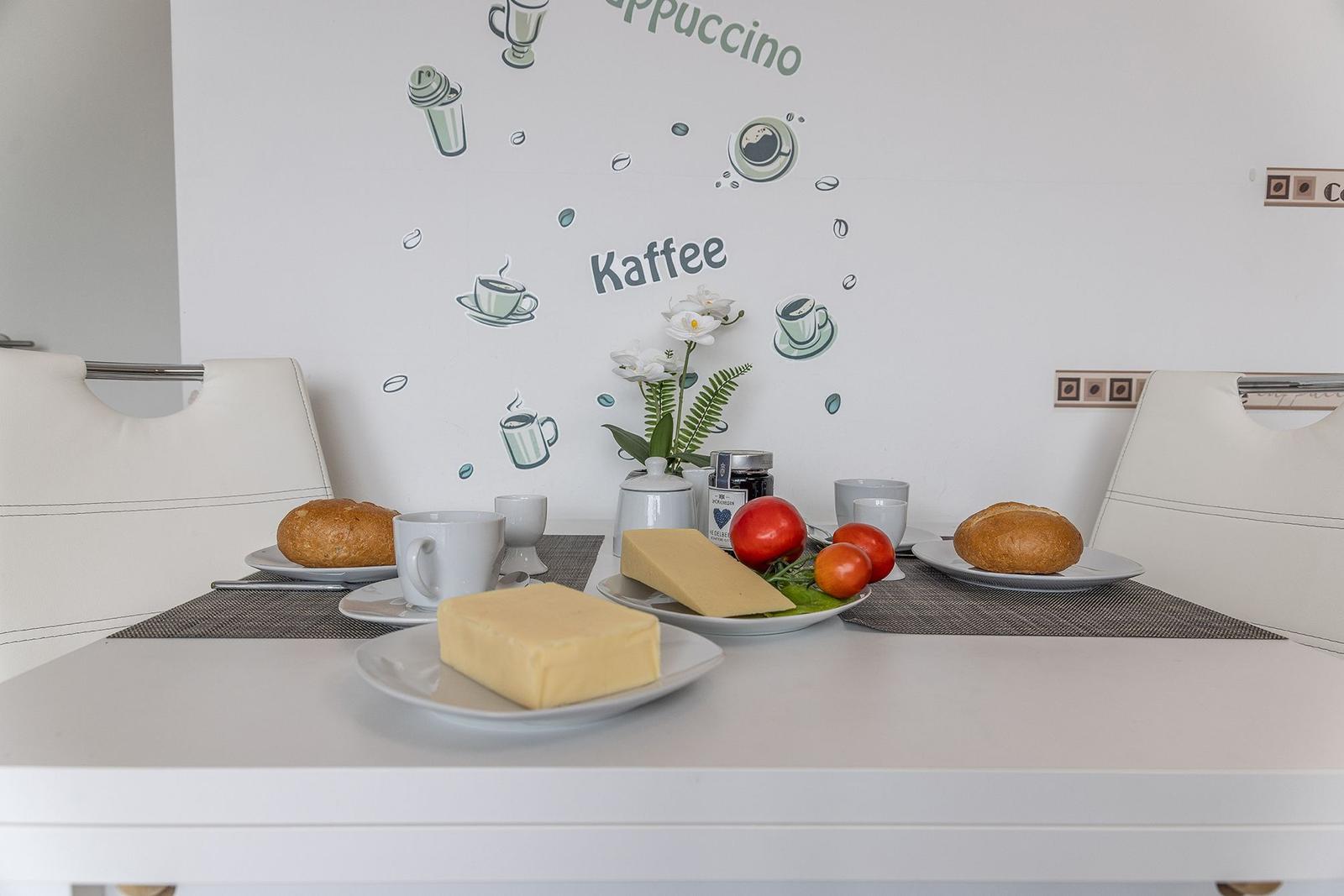 Tisch mit Frühstück, Kaffee und Käse. Wanddekoration mit Kaffee-Motiven.