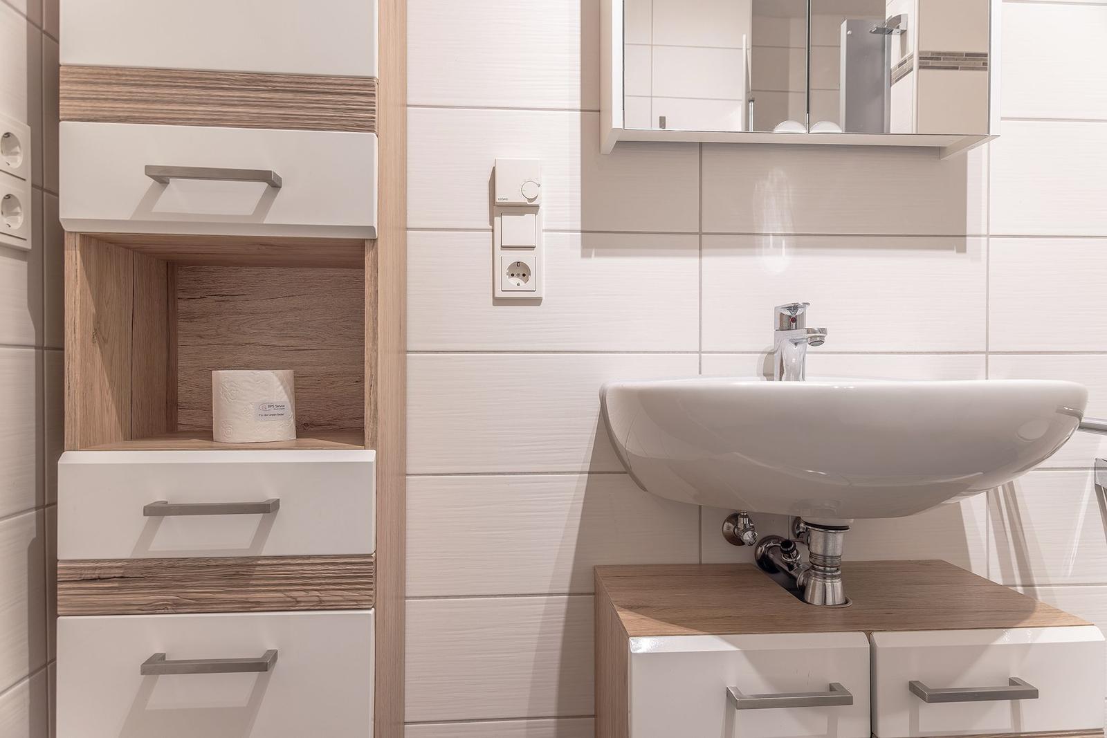 Badezimmer mit Waschbecken, Spiegelschrank und Holz-Weiß-Schränken.