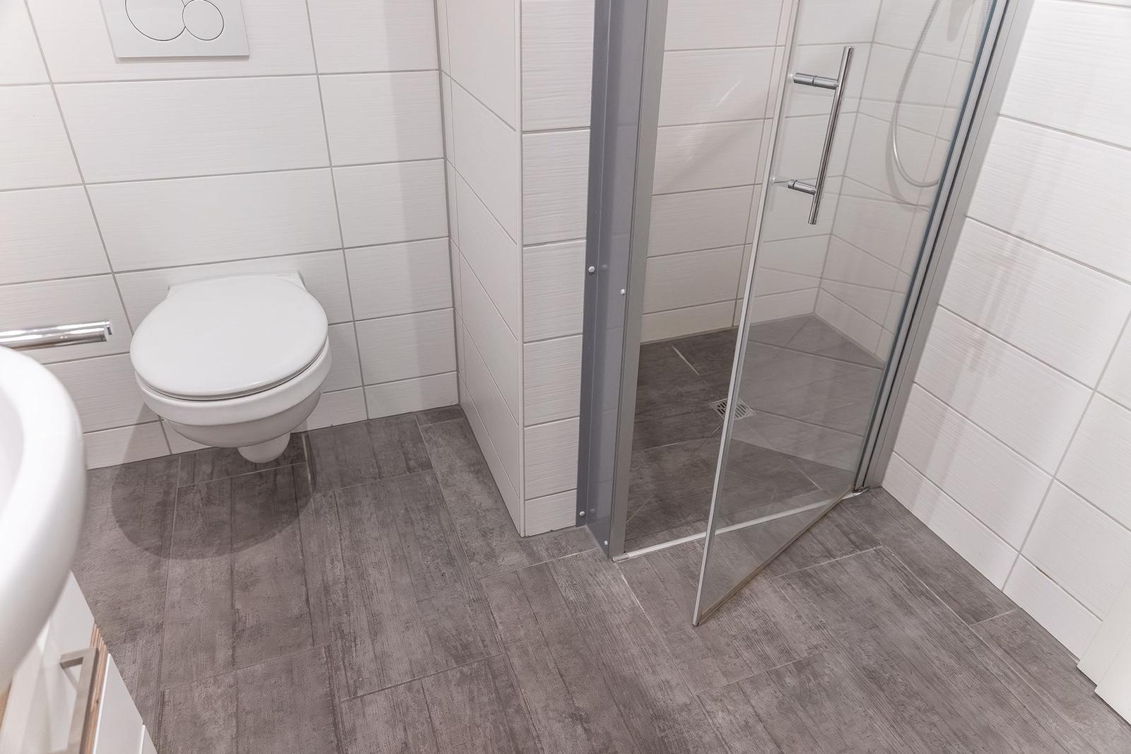 Badezimmer mit Dusche, Toilette und Waschbecken. Fliesenboden und weiße Wände.