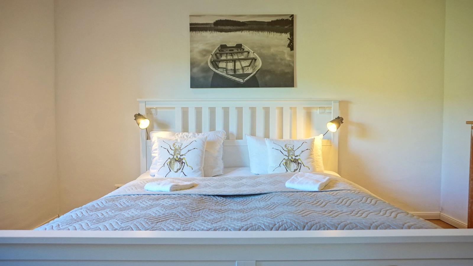 Schlafzimmer mit weißem Bett, Kissen mit Insektenmotiv und Wandbild einer Boot.