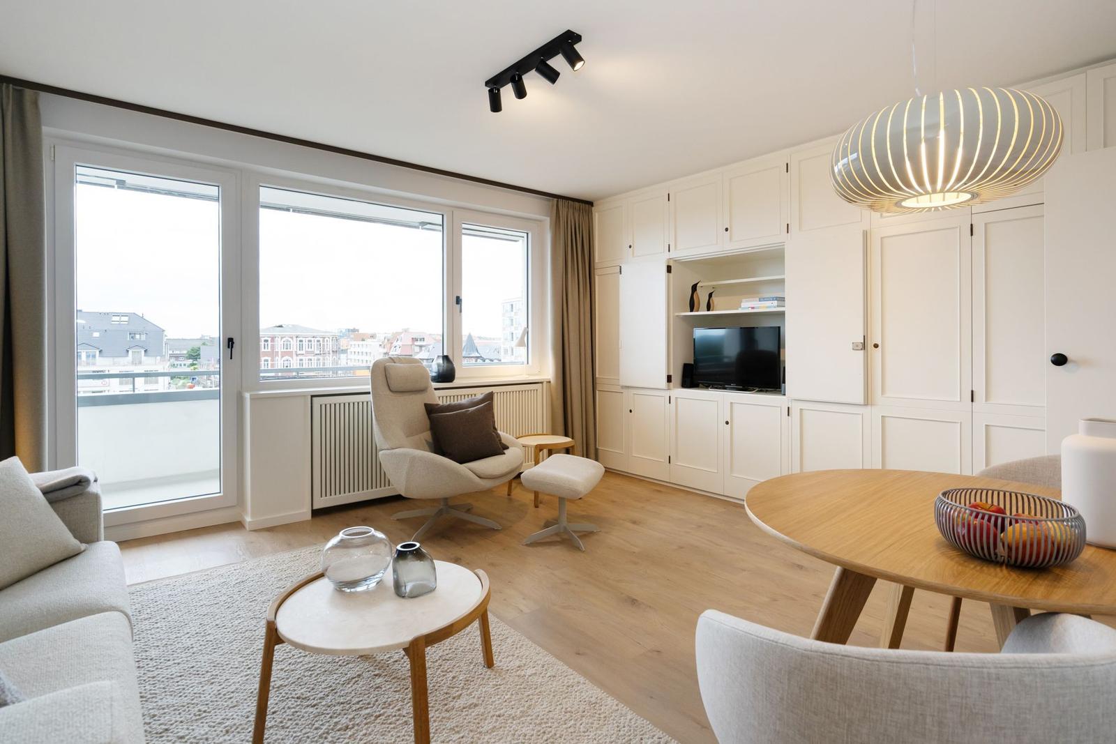 Wohn- und Essbereich mit Balkon, TV und Holztisch.