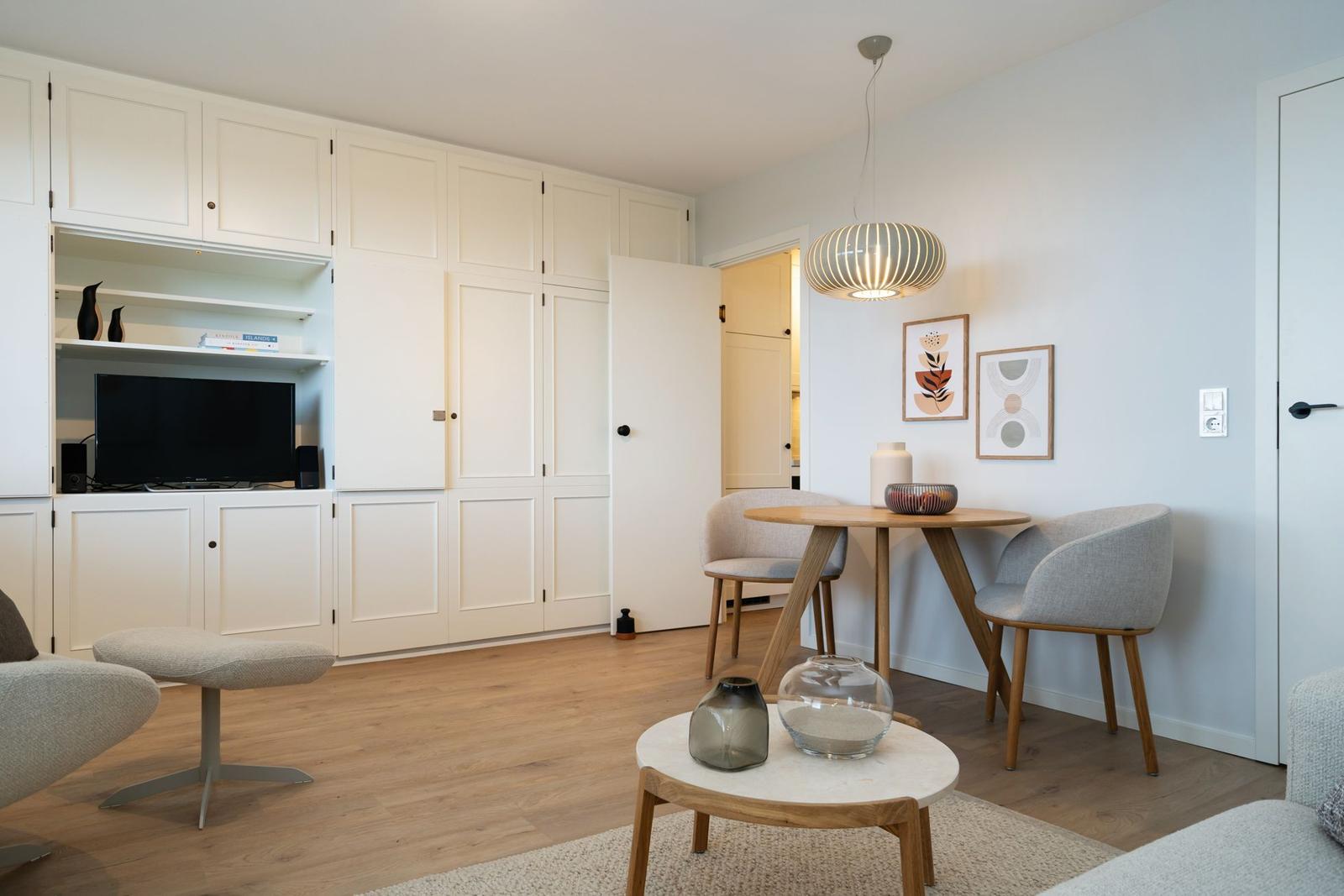 Wohnzimmer mit Essbereich, TV-Einbauwand und Holzboden.