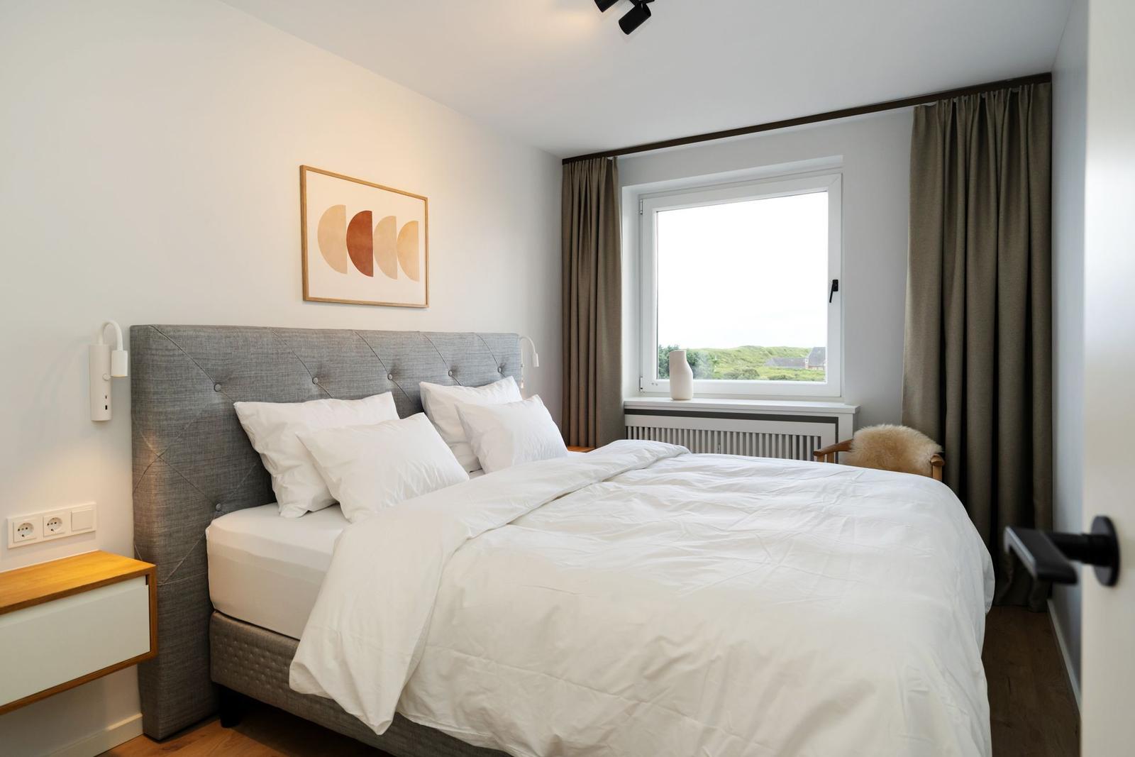 Schlafzimmer mit Bett, Fenster und Wandbild.