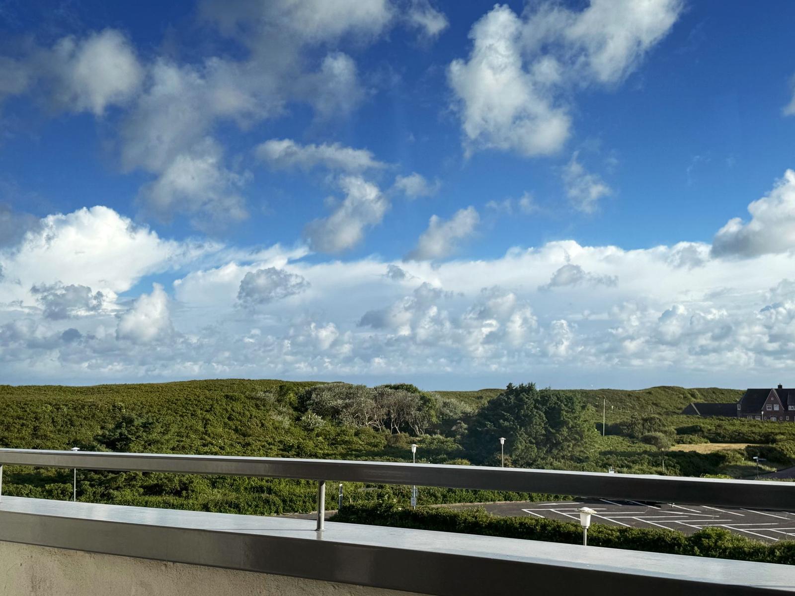 Balkon mit Blick auf grüne Hügel und blauen Himmel mit weißen Wolken.