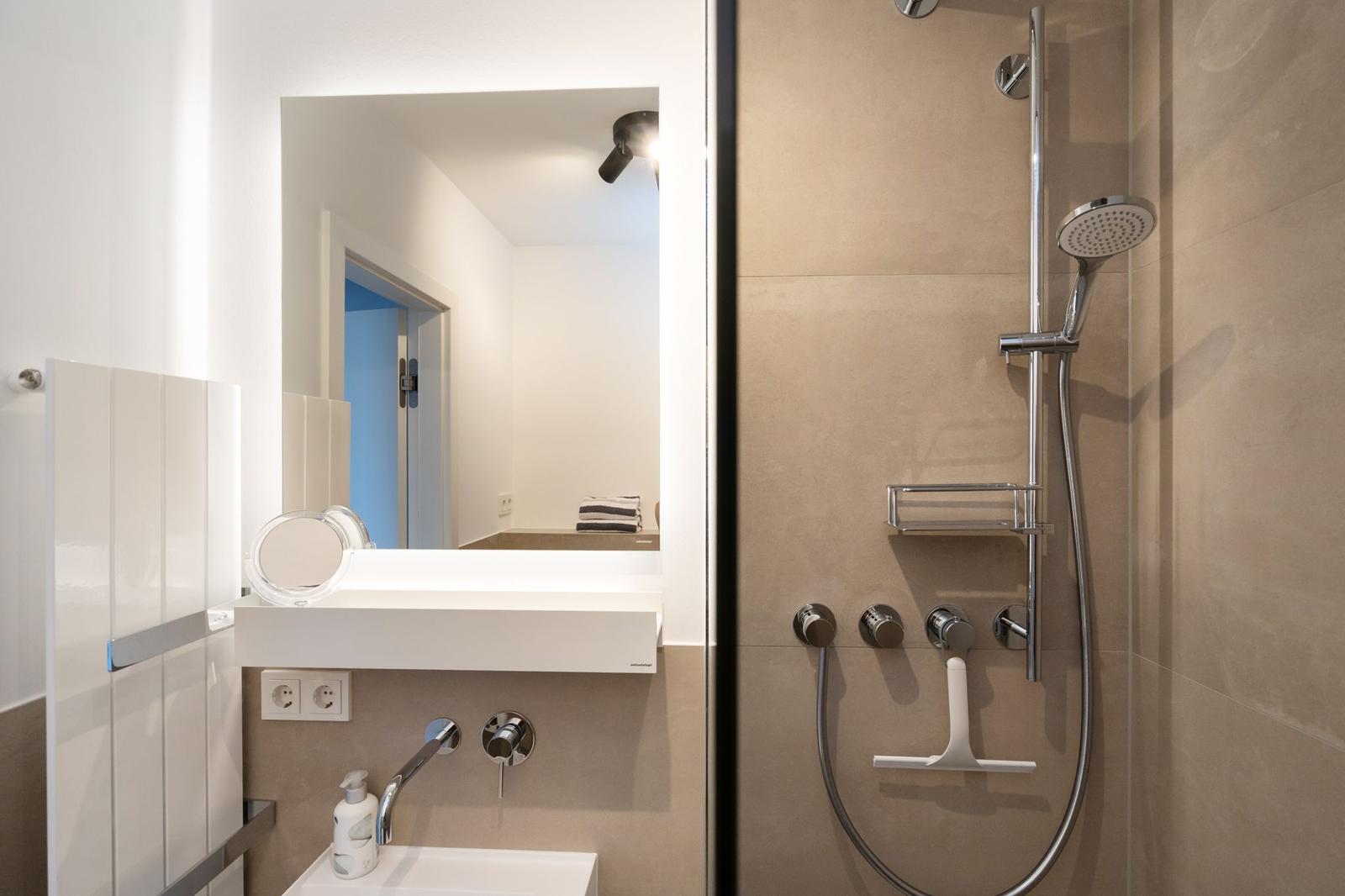 Badezimmer mit Dusche, Waschbecken und Spiegel. Moderne Einrichtung mit Chrom und Weiß.