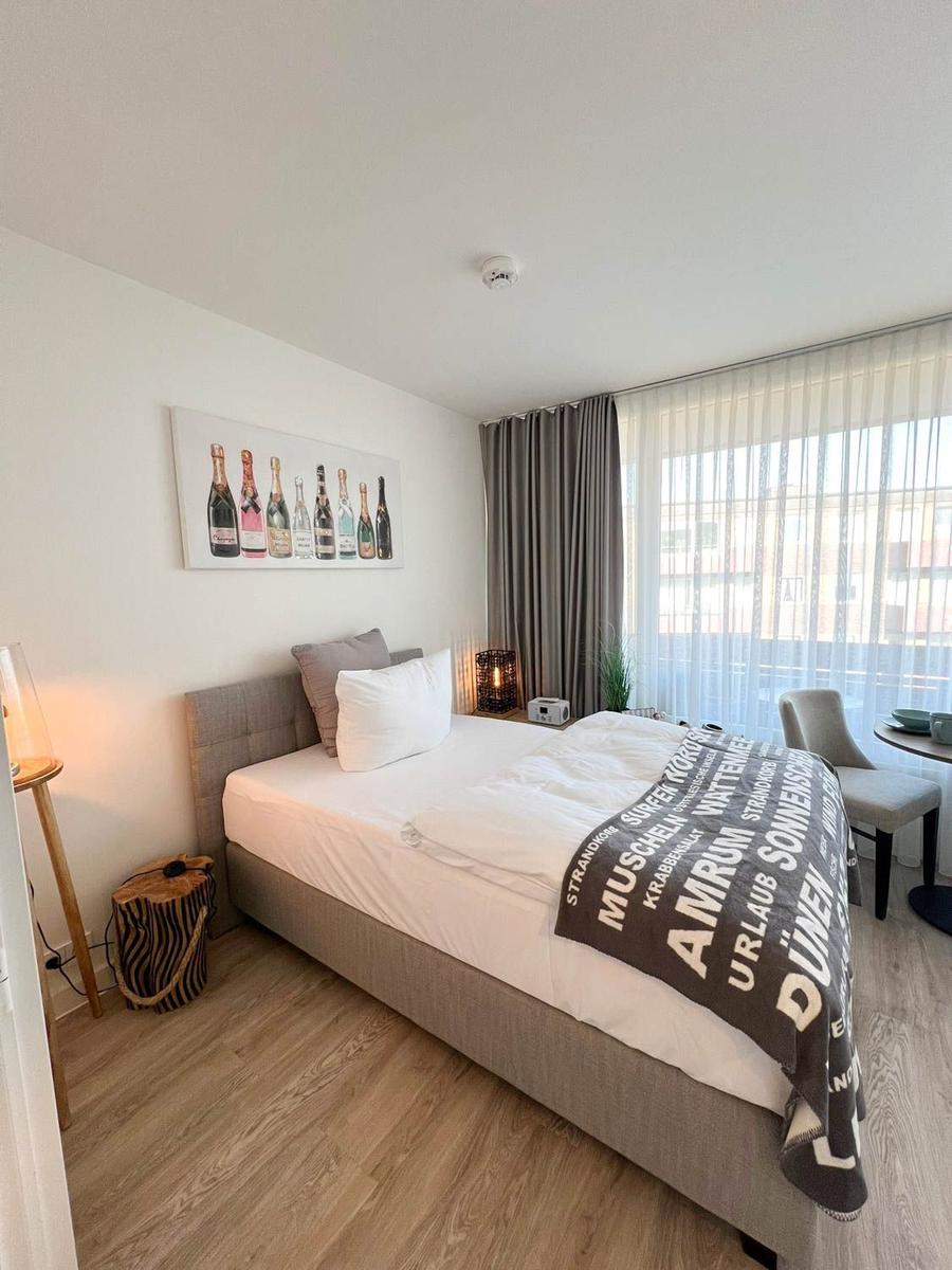 Schlafzimmer mit Bett, Wandbild und Fenster mit Vorhängen.