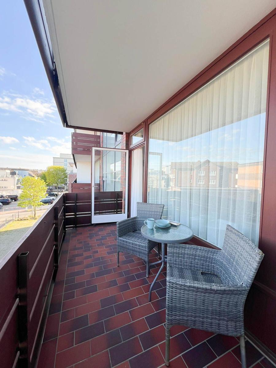 Balkon mit Tisch und zwei Stühlen, roter Fliesenboden und Blick auf die Straße.
