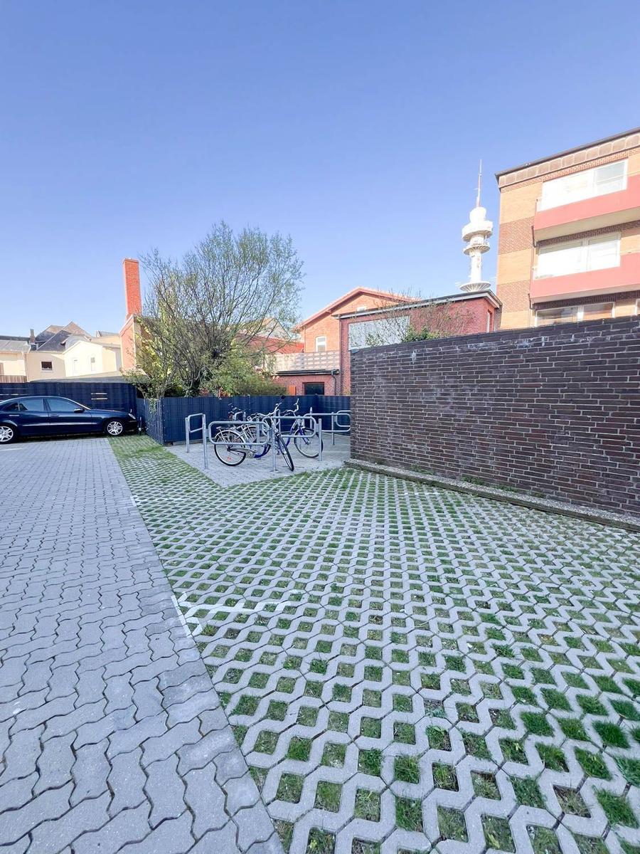 Hinterhof mit Fahrradständer, gepflastertem Bereich und Mauer. Ein Auto parkt daneben.