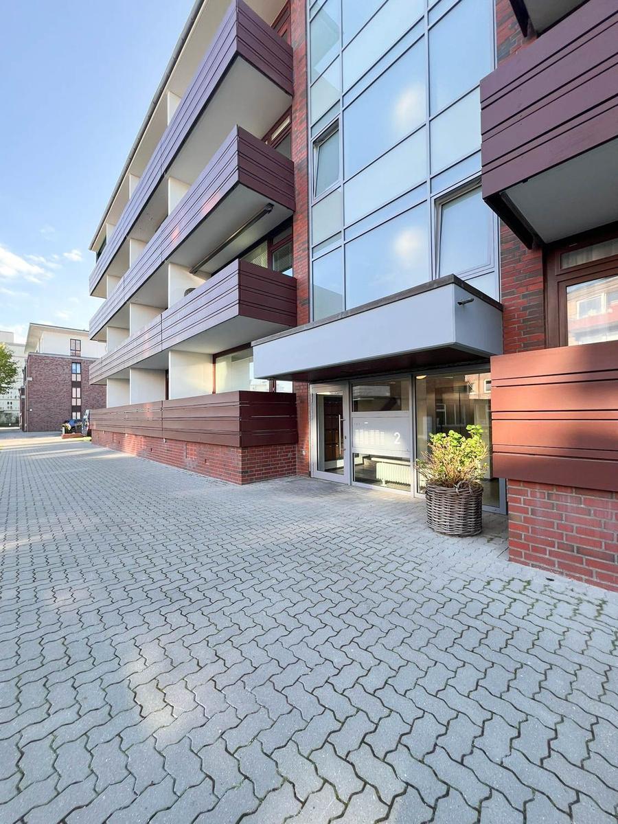 Eingangsbereich eines modernen Mehrfamilienhauses mit Glasfassade und Holzverkleidung.