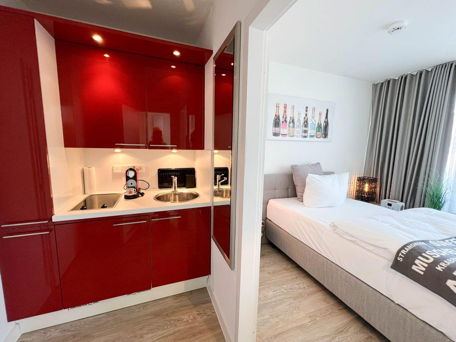 Küche mit roten Schränken und Schlafzimmer mit Bett und Vorhängen.