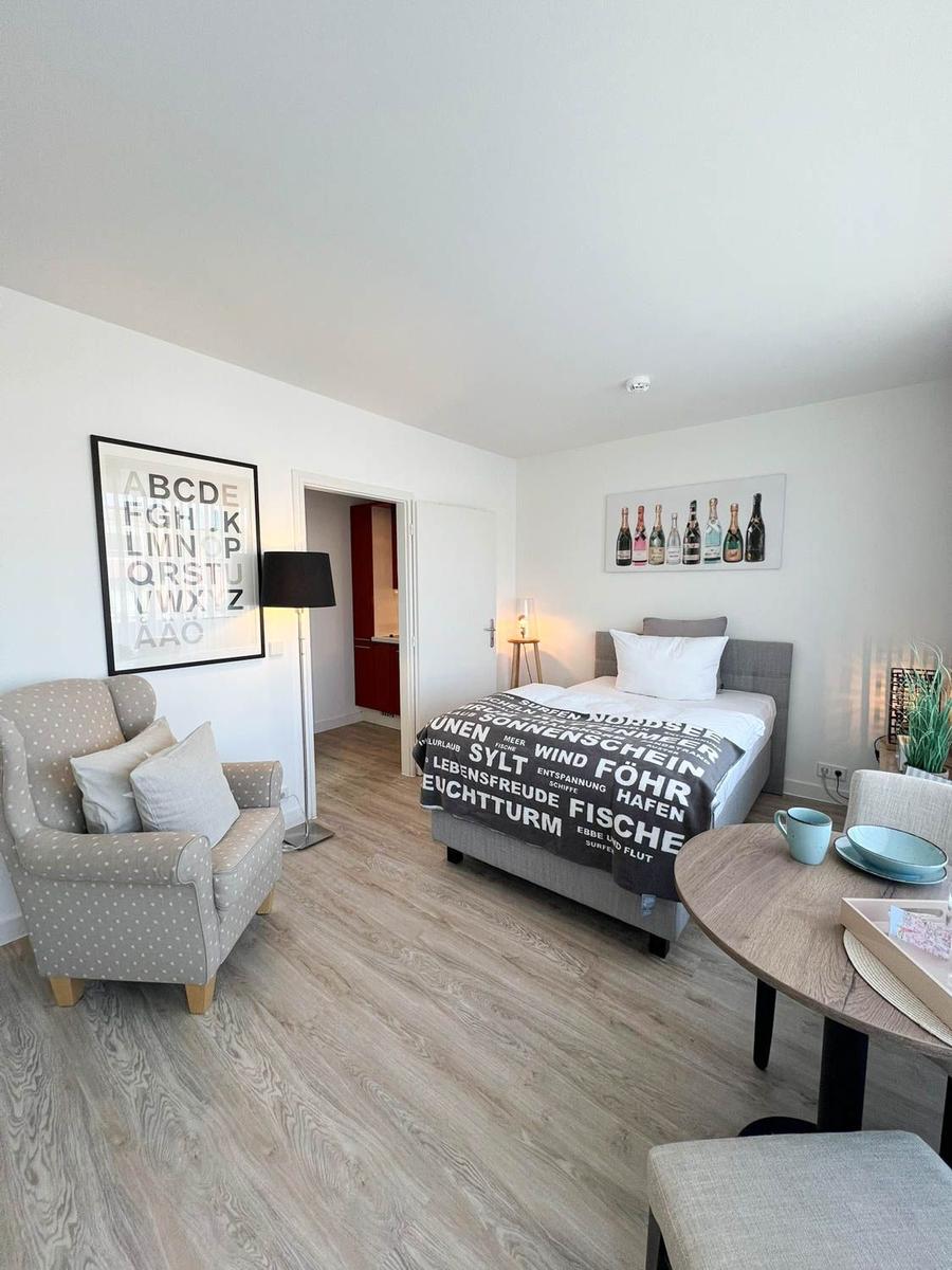 Schlafzimmer mit Bett, Sessel und Tisch. Wandbilder und Holzboden.