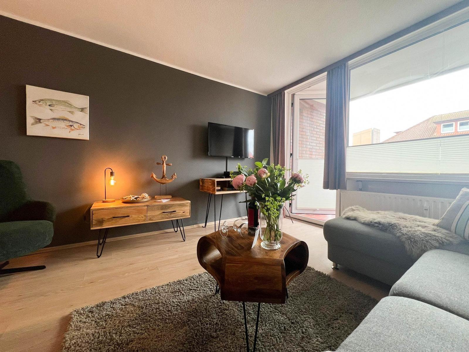 Wohnzimmer mit Sofa, Couchtisch, Fernseher und Fenster zur Terrasse.