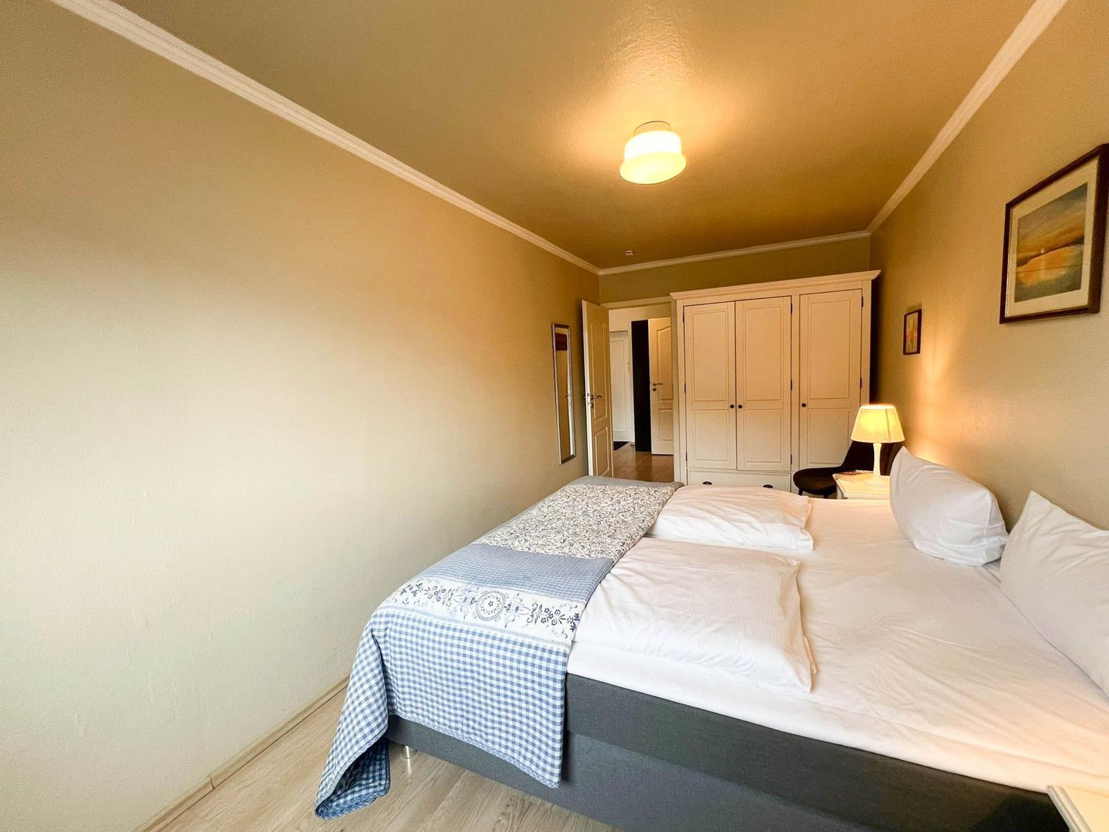 Schlafzimmer mit Doppelbett, Kleiderschrank und Nachttisch mit Lampe.