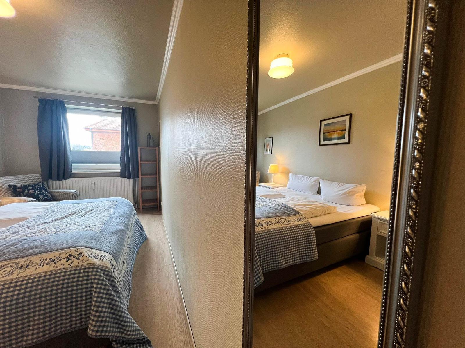 Schlafzimmer mit Bett, Spiegel und Fenster. Holzboden und Wanddekoration.