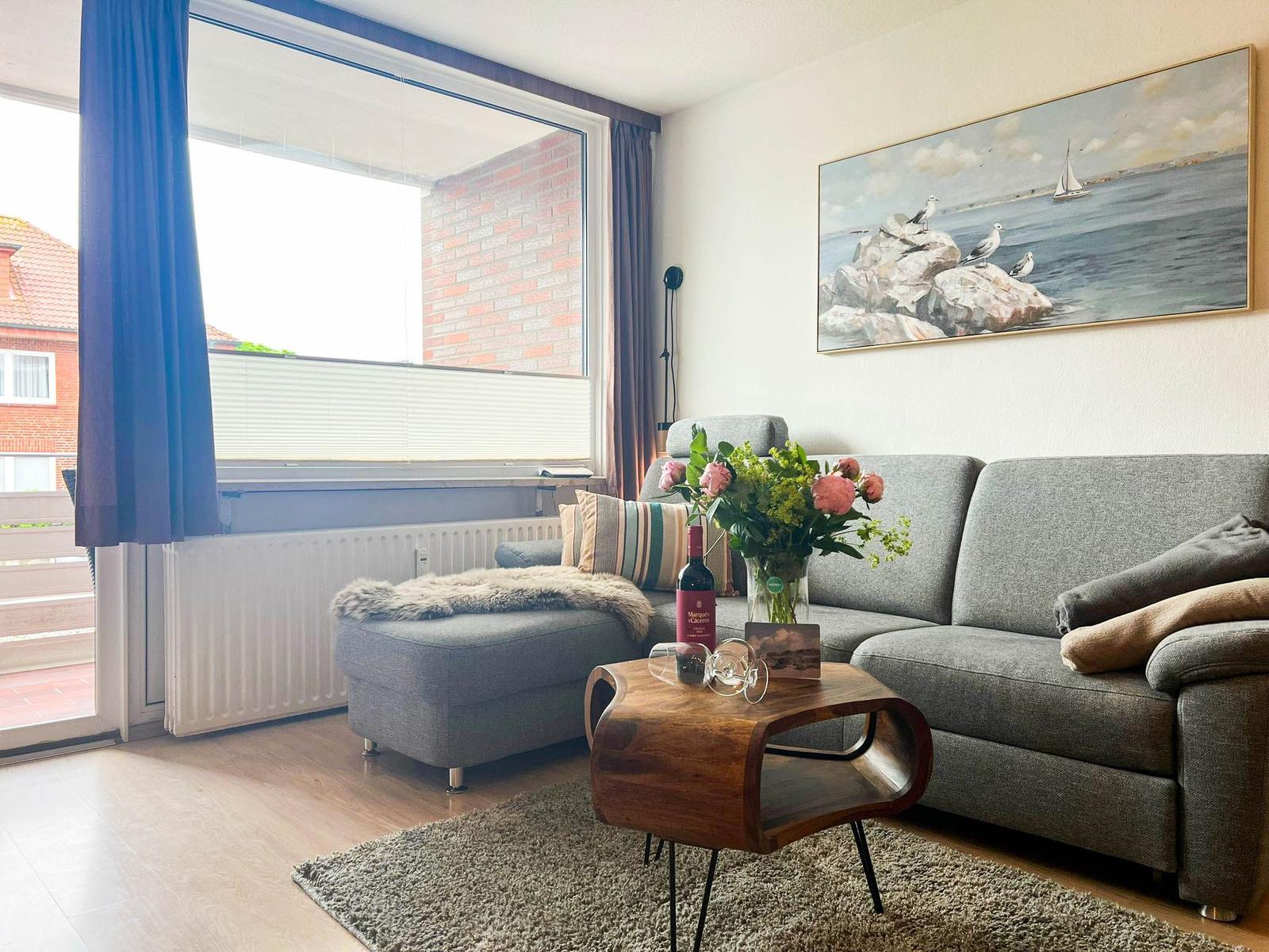Wohnzimmer mit grauem Sofa, Holztisch und Wandbild mit See.
