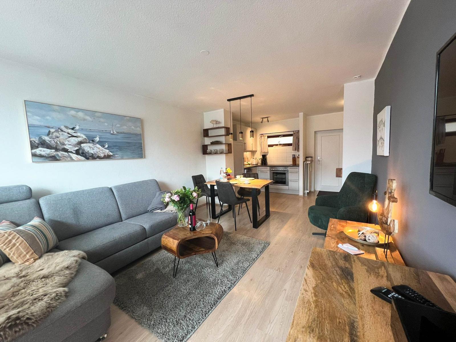 Wohnzimmer mit Sofa, Esstisch und Küche im Hintergrund.