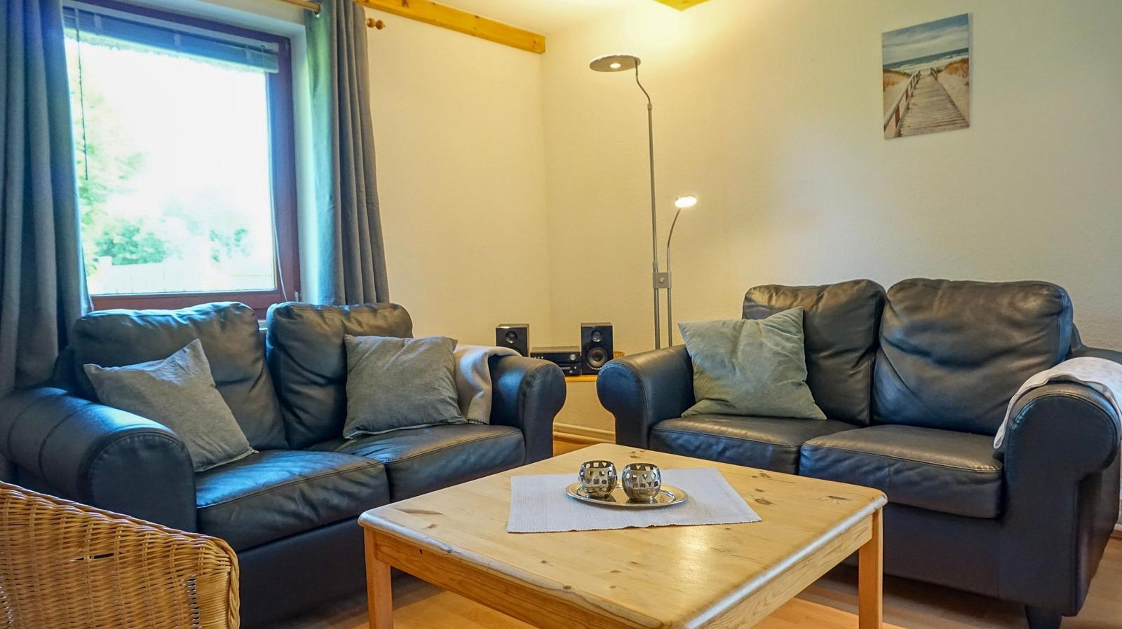 Two leather sofas, wooden table, window with curtains, floor lamp, and wall picture.
