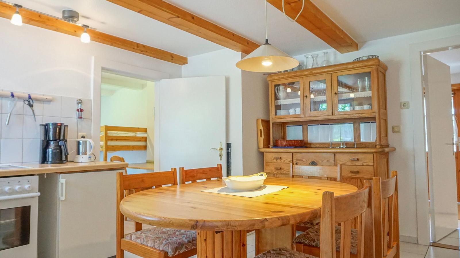 Dining area with round table and wooden chairs. Kitchen counter and glass cabinet are visible.