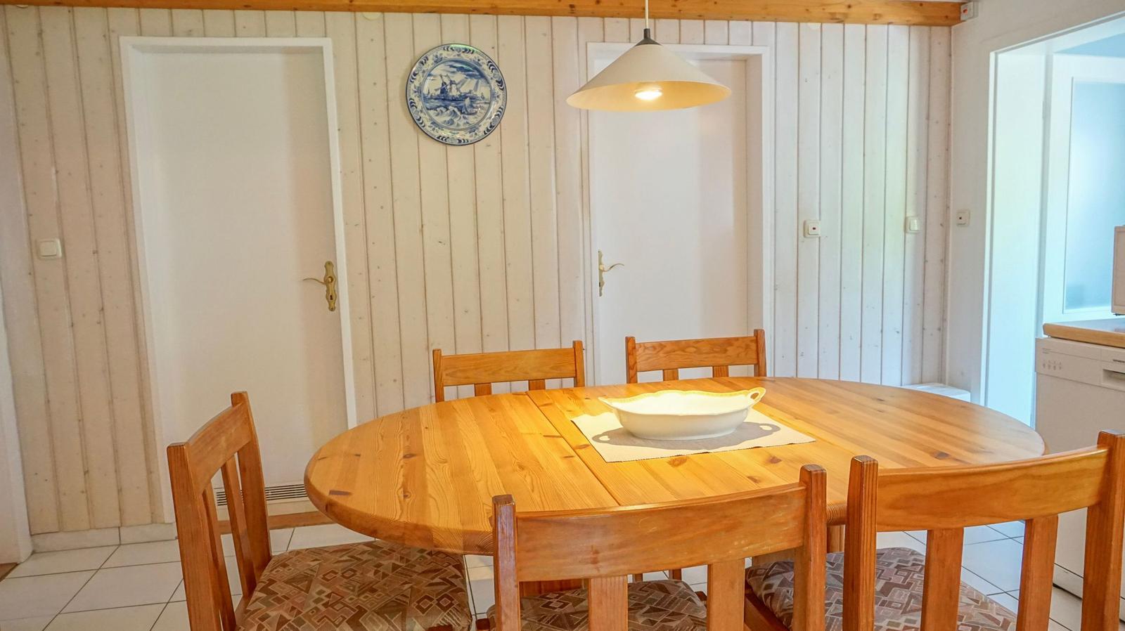Round wooden table with chairs and a bowl. A blue plate hangs on the wall.