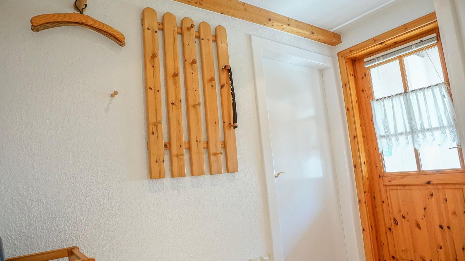 Wall with wooden coat rack, door, and window with curtain.