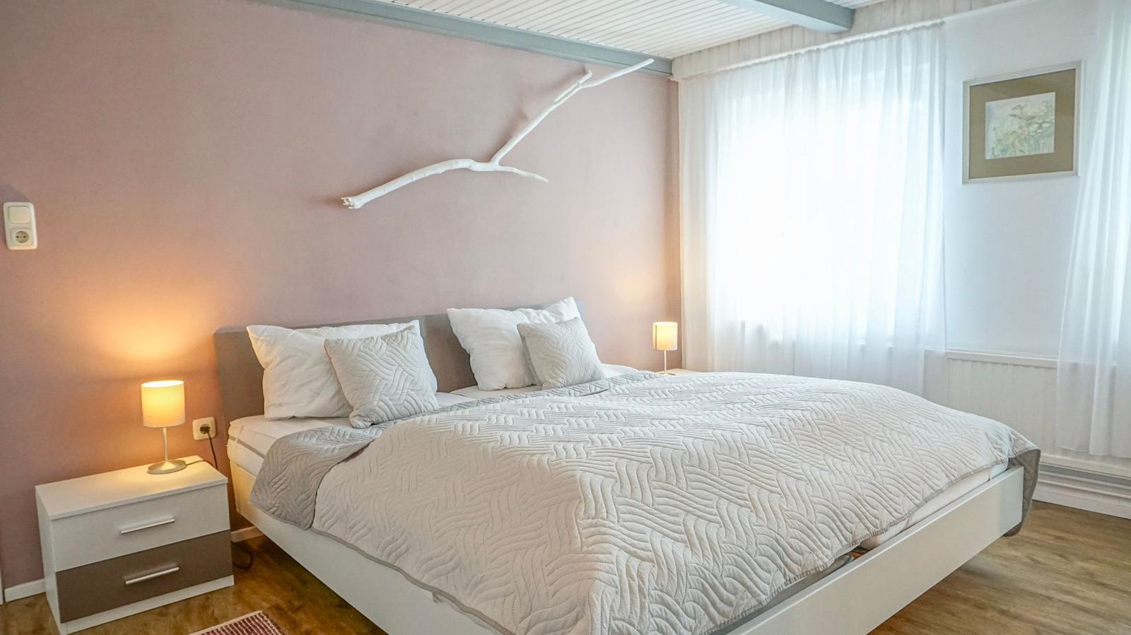 Bedroom with bed, nightstand, and lamp. Wall decor and window with curtains.