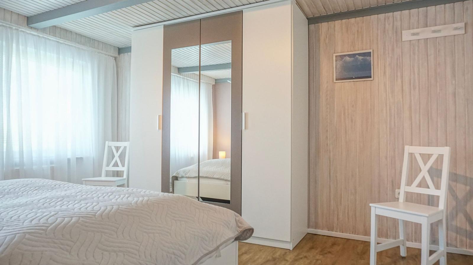 Bedroom with bed, wardrobe, and two white chairs.