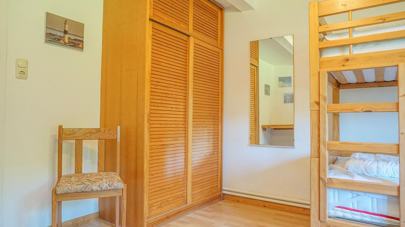 Bedroom with wooden bunk bed, wardrobe, and mirror on the wall.