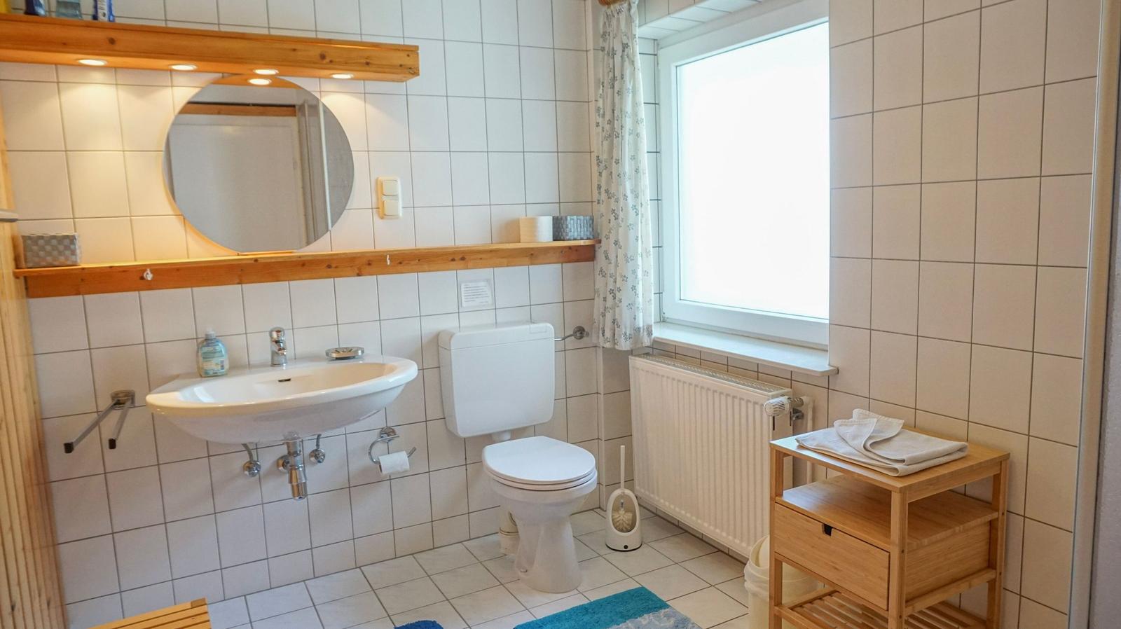 Bathroom with sink, toilet, and window. Wooden shelves and mirror.