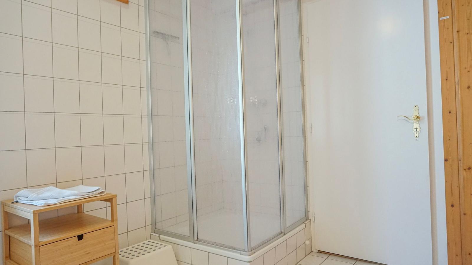 Bath with shower, wooden shelf, and white door