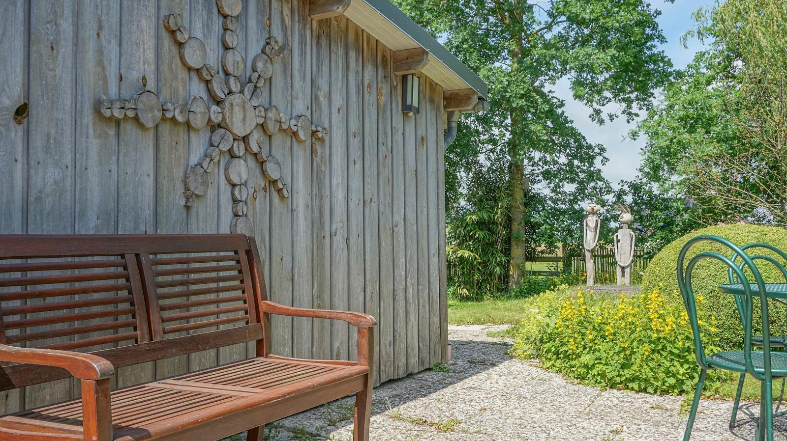 Wooden bench in front of rustic wooden house with garden path and sculptures.