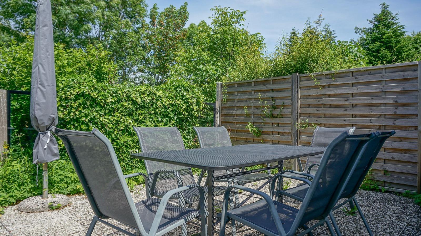 Outdoor area with table and chairs, surrounded by greenery and wooden fence.