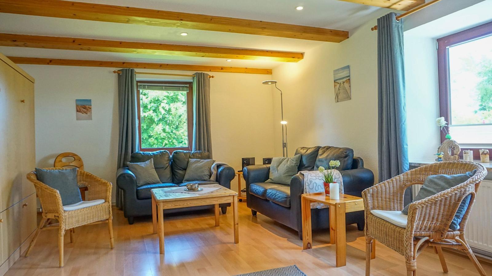Living room with two sofas, two chairs, and wooden floor. Wooden ceiling beams and windows with curtains.