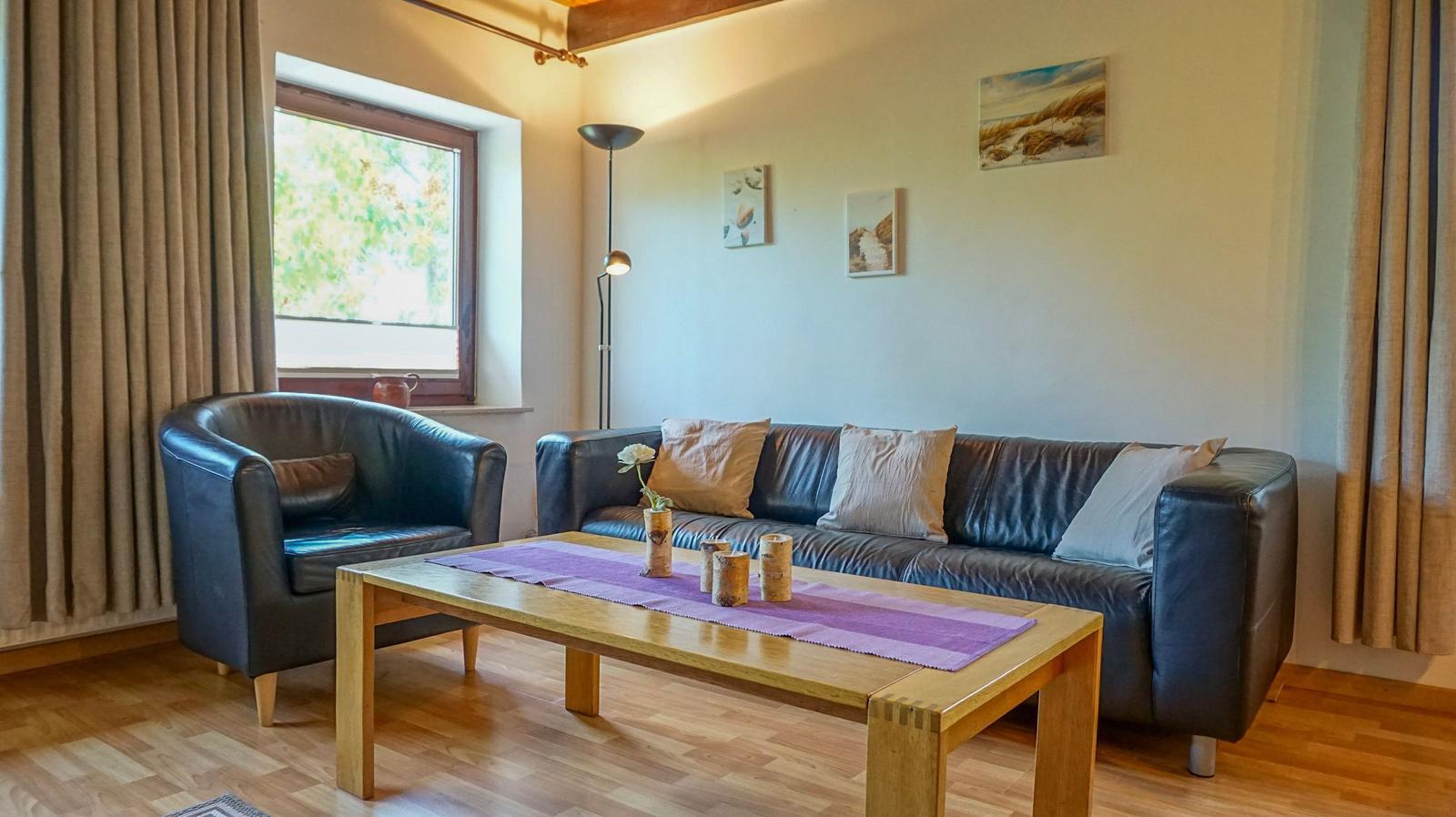 Wohnzimmer mit Ledersofa, Holztisch und Fenster mit Blick nach draußen.
