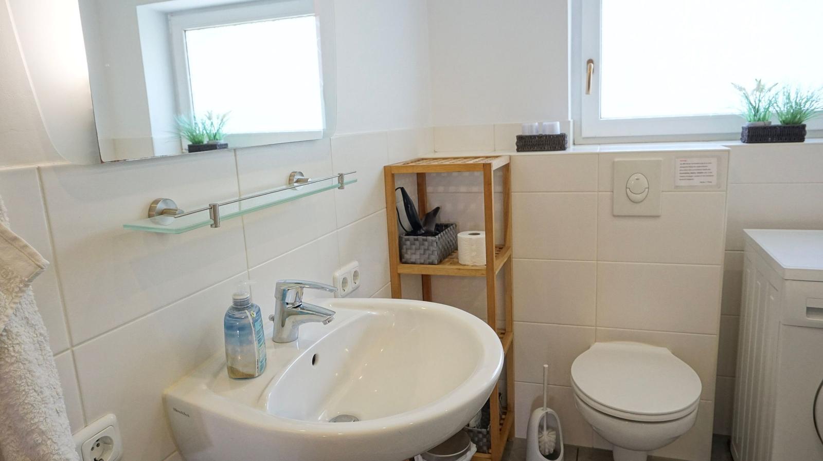 Badezimmer mit Waschbecken, Spiegel, Toilette und Holzregal.