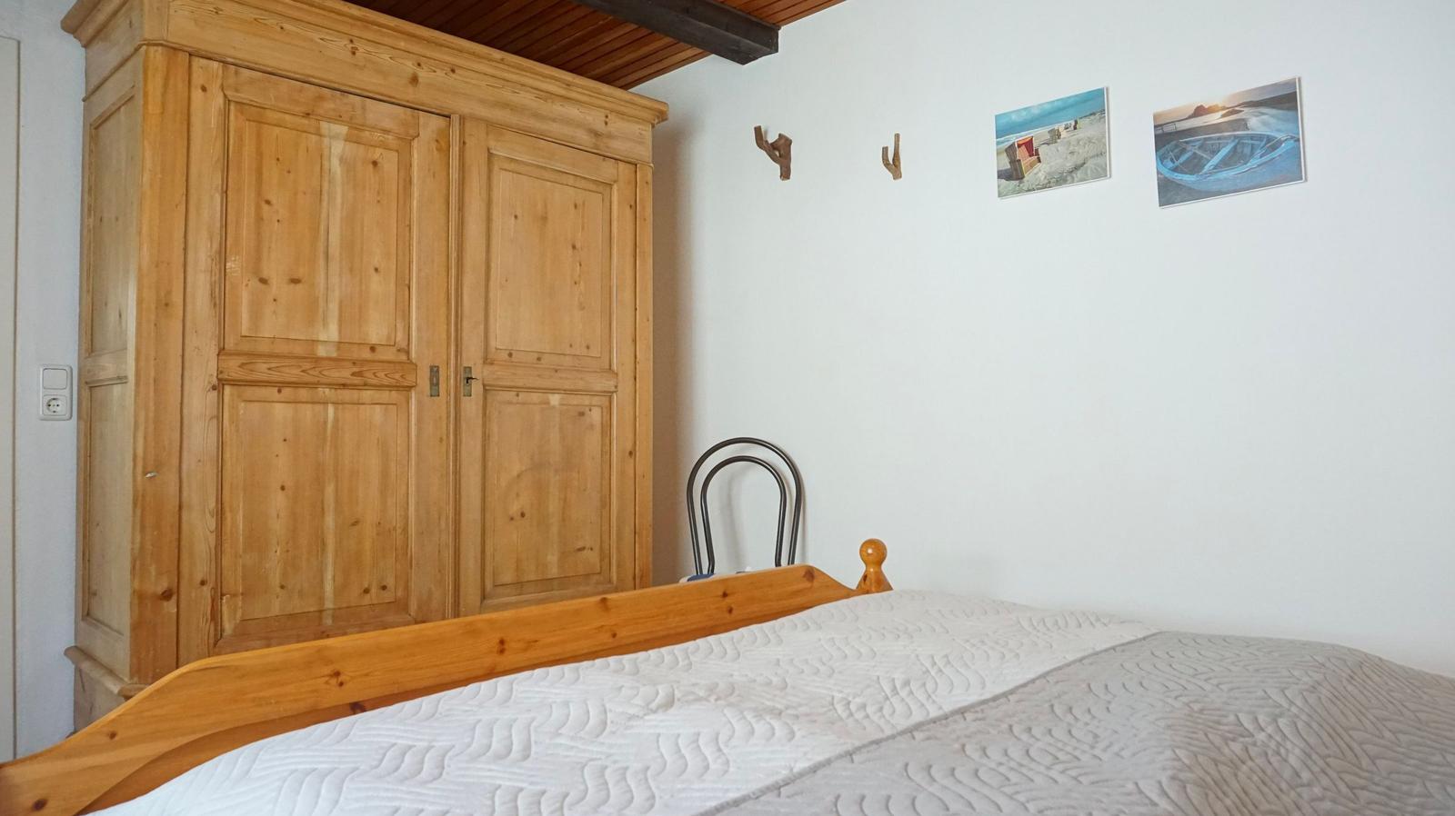 Schlafzimmer mit Holzschrank, Bett und Wandbildern.