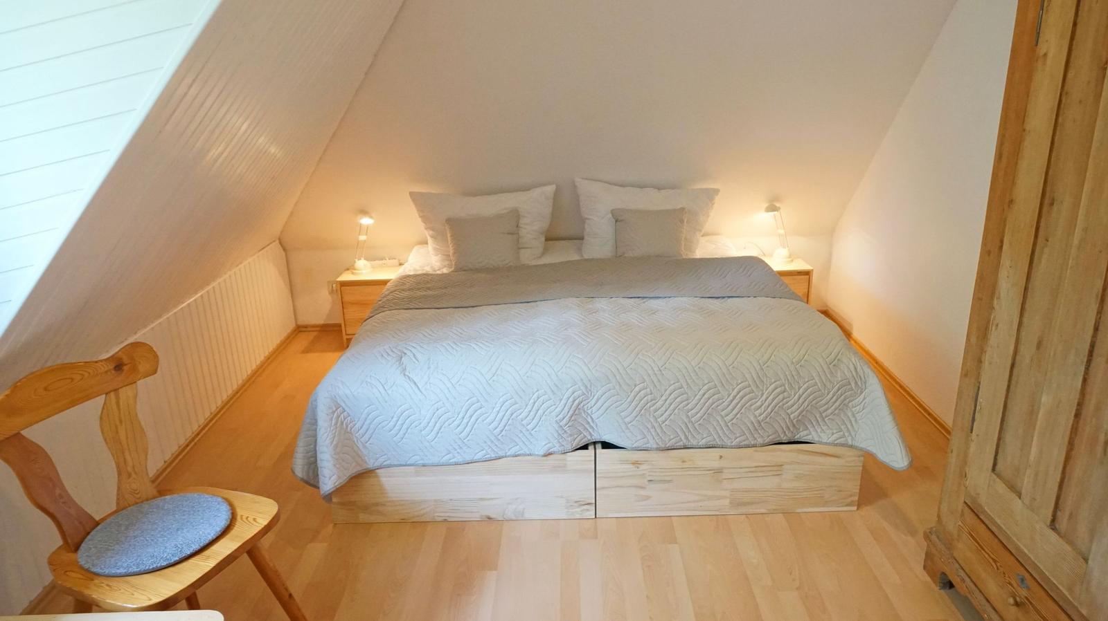 Schlafzimmer mit Dachschrägen, Holzboden, Bett und Nachttischen.