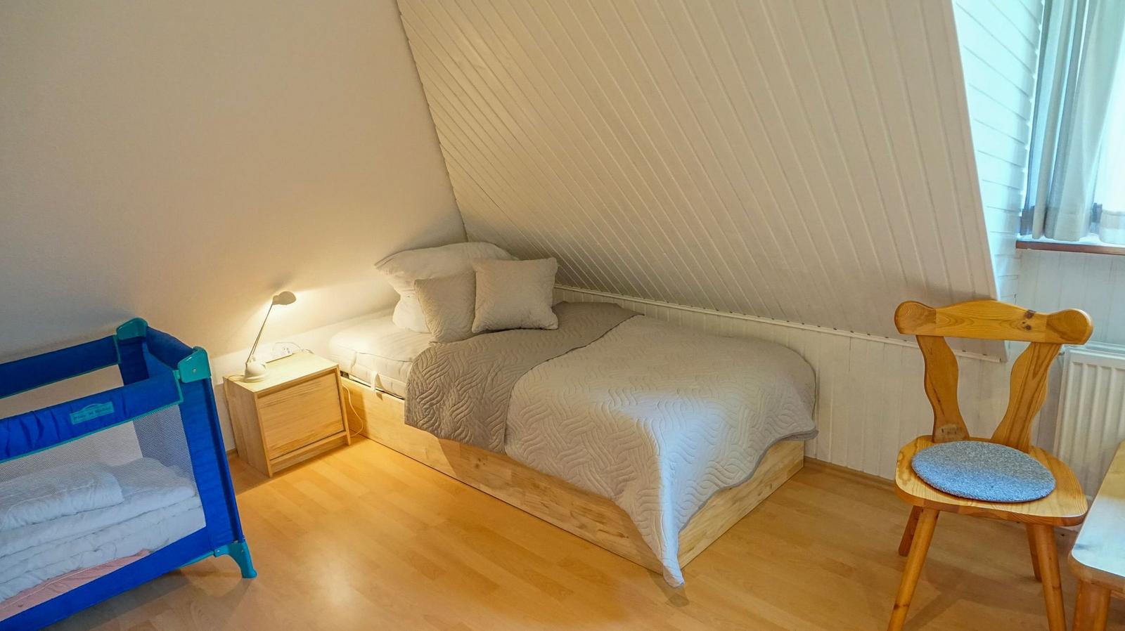 Schlafzimmer mit Bett, Kinderbett, Stuhl und Nachttisch unter schrägem Dach