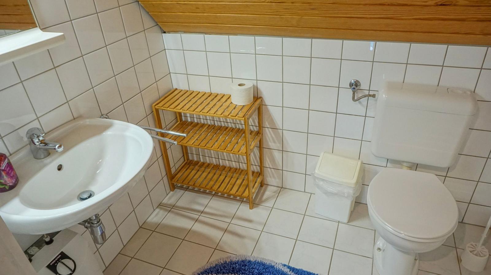 Badezimmer mit Toilette, Waschbecken und Holzregal.