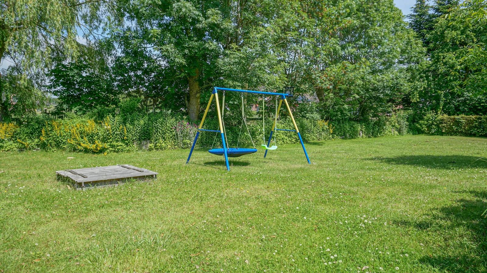 Garten mit Schaukel und Holzterrasse. Umgeben von Bäumen und Gras.