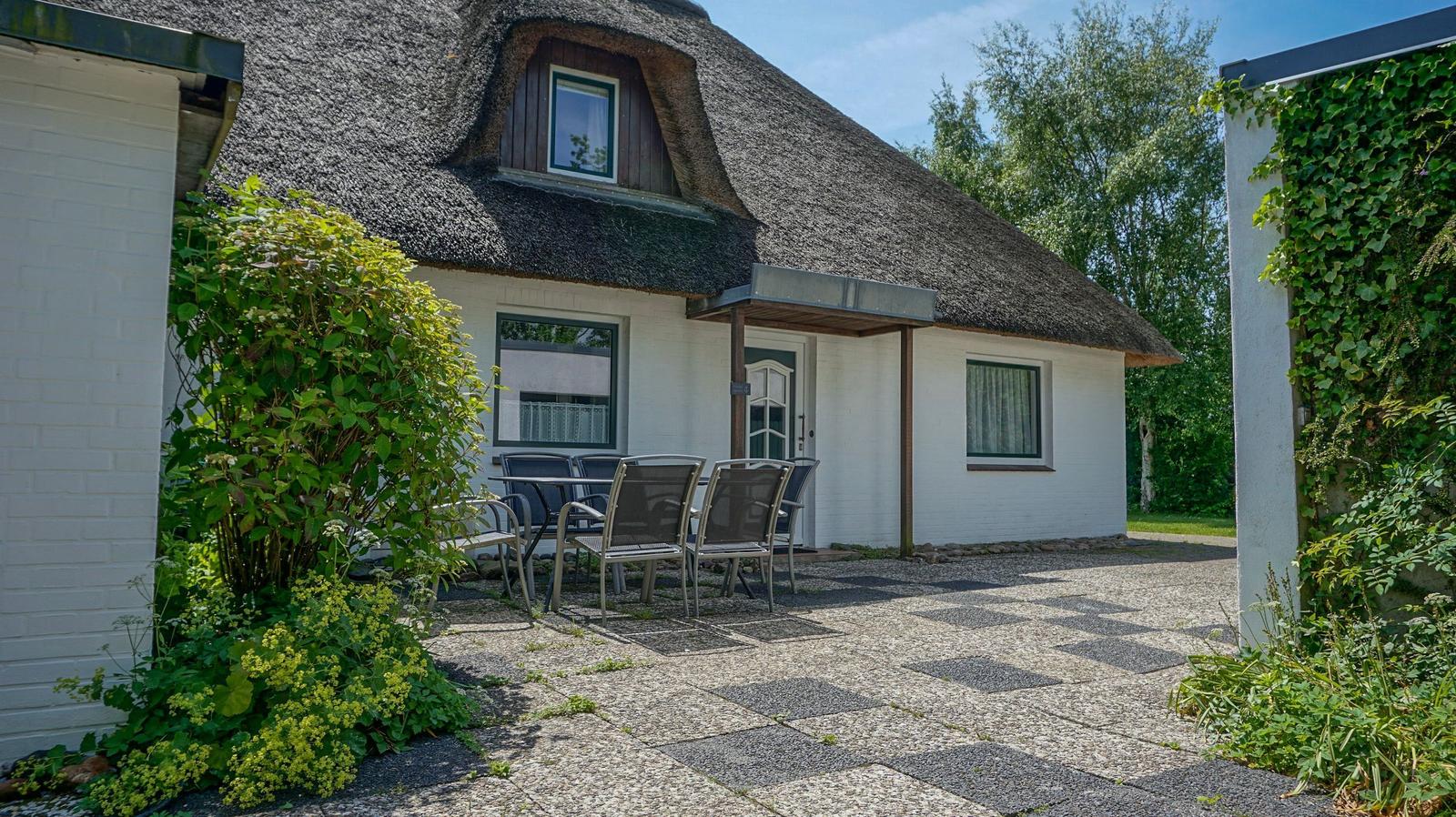 Haus mit Strohdach, weißer Fassade und Gartenbereich mit Sitzgelegenheit.