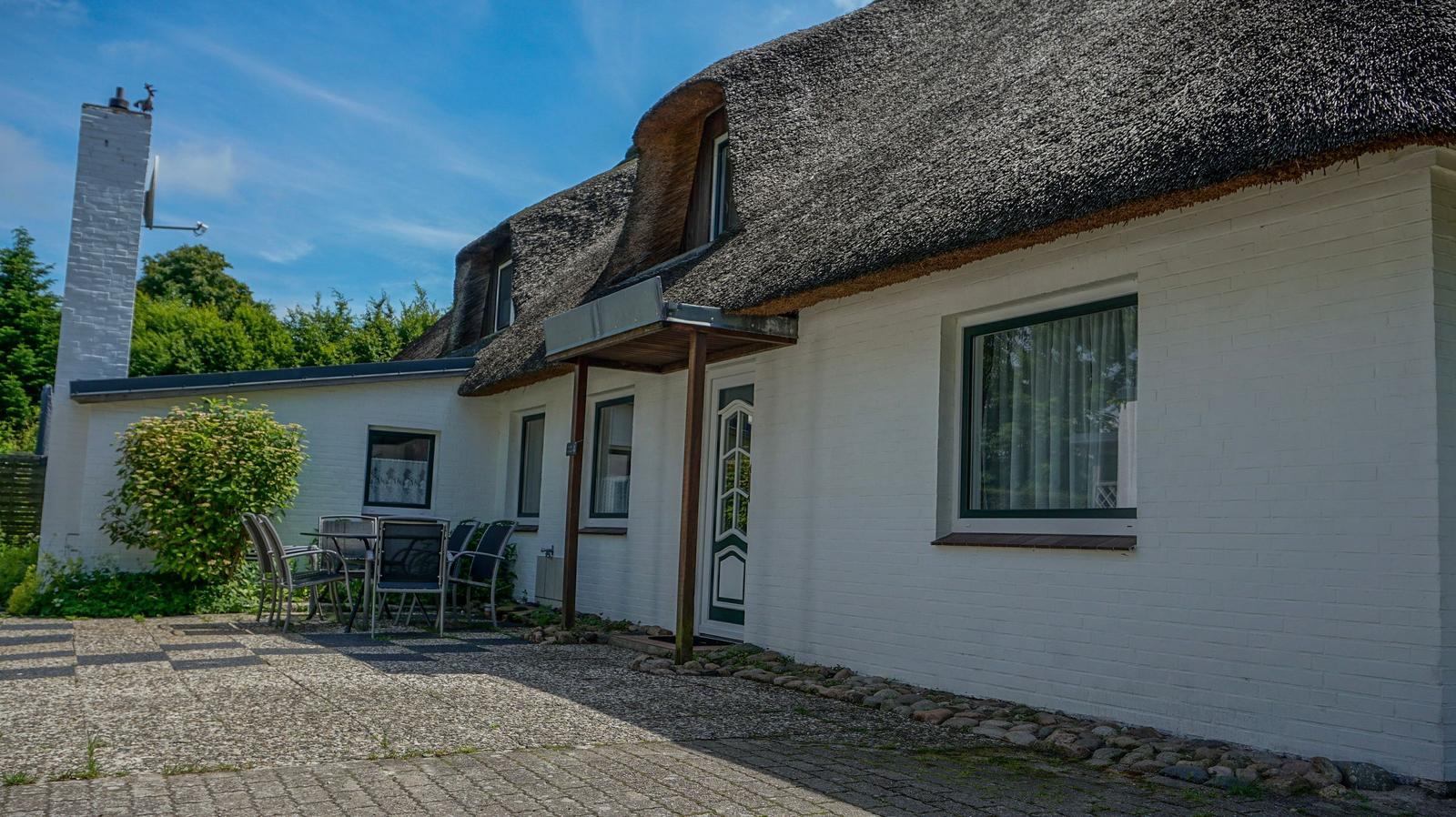 Wohnhaus mit strohgedecktem Dach und weißer Fassade. Außenterrasse mit Tisch und Stühlen.