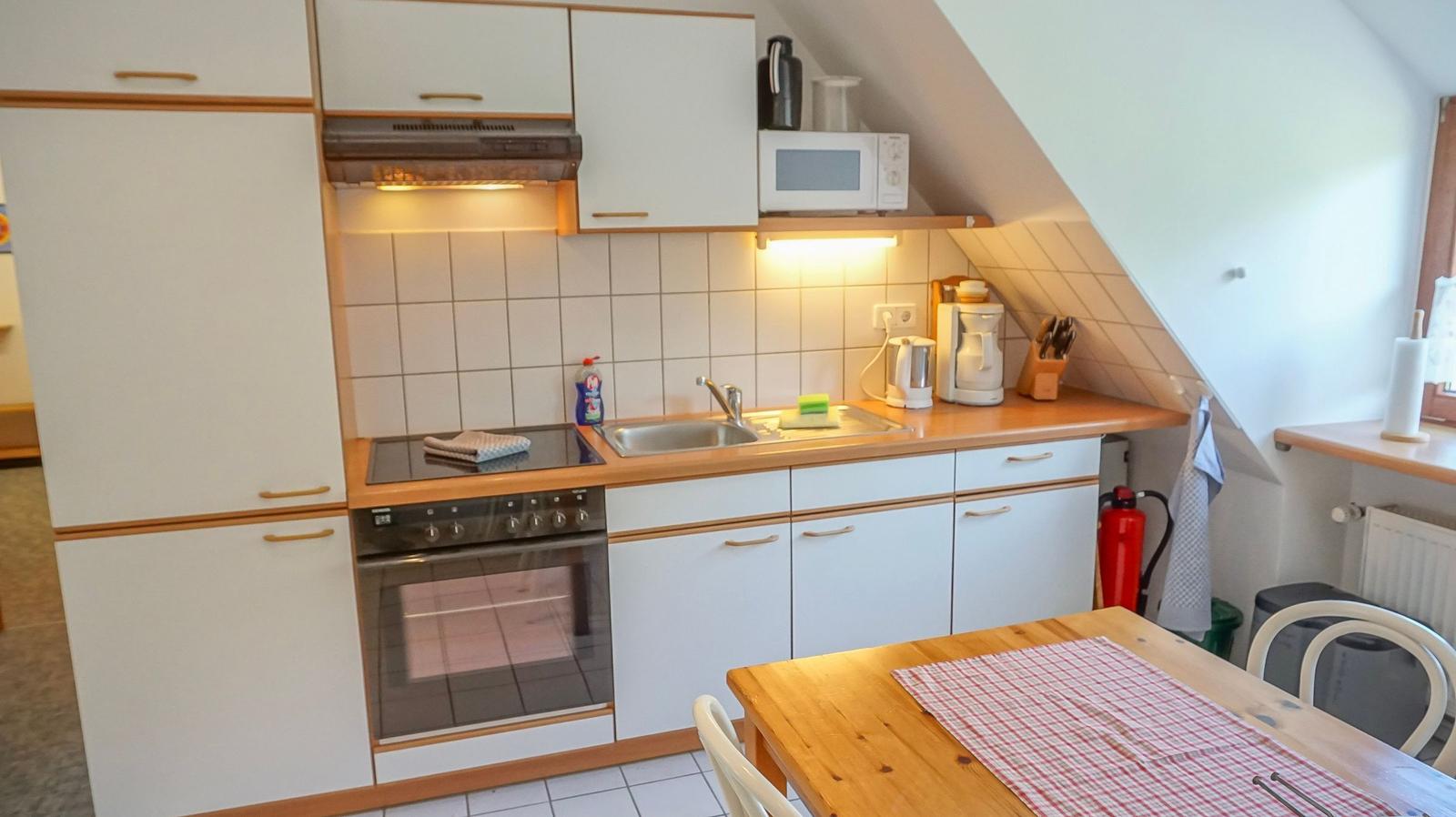 Kitchen with wooden countertop, white cabinets, and built-in oven. Dining table with tablecloth.