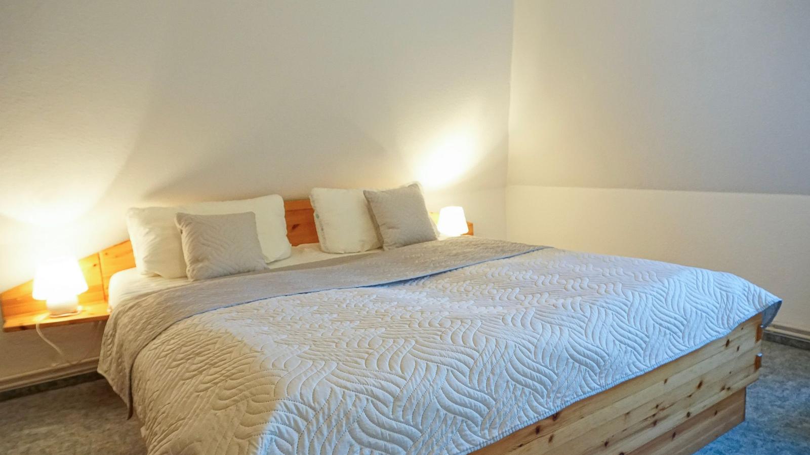A bedroom with a wooden bed, a quilt, and two nightstands with lamps.