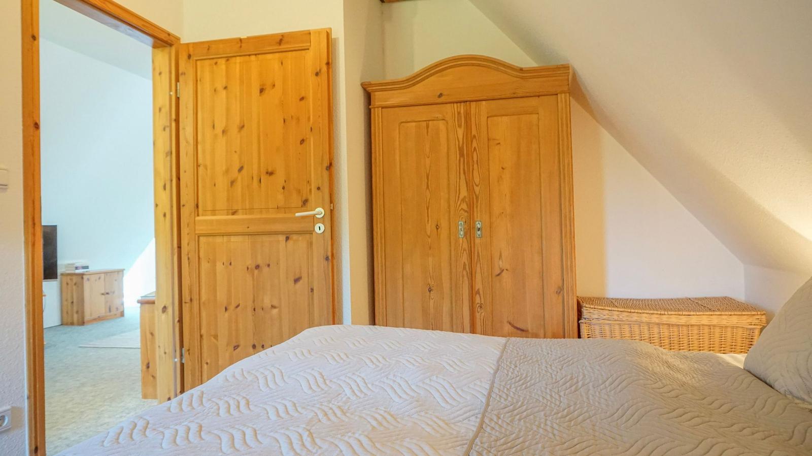 Bedroom with wooden wardrobe, bed, and door to hallway. Sloped ceiling on wall.
